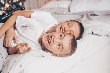 Fototapeta na wymiar Happy family New Year concept. Two cute smiling kids brothers having fun, laughing and hugging on the white bed against the background of the Christmas tree