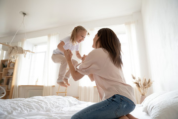 Happy mother and little daughter having fun, jumping on bed