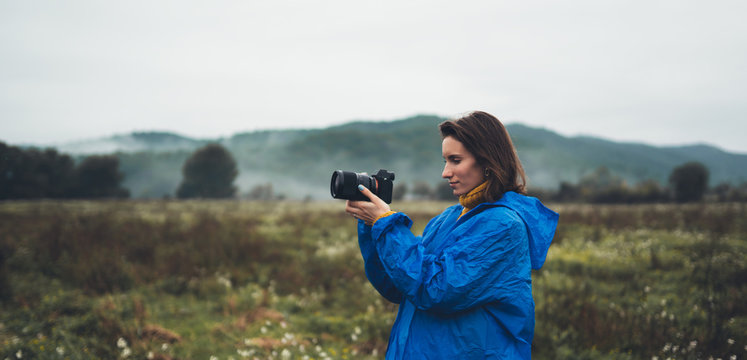 photographer tourist girl in blue raincoat hold in hands photo camera take photography foggy mountain, traveler shooting nature, click on camera technology, landscape vacation concept free space