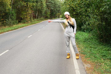 A young and beautiful girl votes on the road. Autumn road. Catch a car on an empty road. Hitchhiking. Free travel by car.