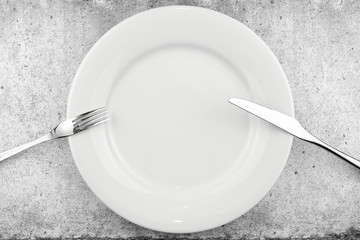 Table setting. Empty plate, knife and fork on a light concrete background. Fork and knife are on the plate, pause in food. Top view and flat lay with copy space.