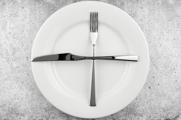 Table setting. Empty plate, knife and fork on a light concrete background. A fork and a knife lie on a plate, waiting for the next dish. Top view and flat lay with copy space