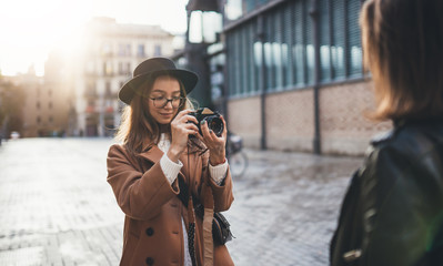 Photographer with camera take photo model girlfriend. Blogger photoshoot concept. Tourist smiling girl travels in Barcelona holiday with traveler friend. Sunlight flare street in europe city