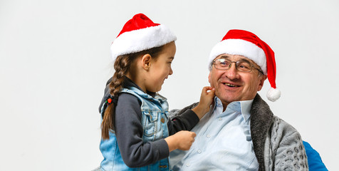 A small girl and senior grandfather with Santa hat hugging at Christmas time.