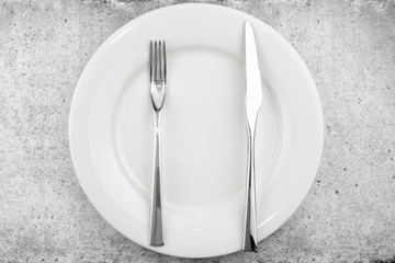 Table setting. Empty plate, knife and fork on a light concrete background The fork and knife lie in parallel on a plate, the meal is finished. Top view and flat lay with copy space