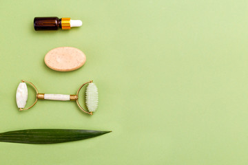 Face roller and beauty product on green background. Copy space. Minimal