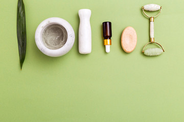 Face roller and skin care products on green background. Copy space. Flat  lay