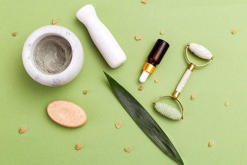 Face roller and skin care products on green background. Flat lay. Background