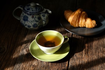 Tea composition. A cup of hot tea, croissant and macaroons on a wooden table background.
