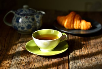 Tea composition. A cup of hot tea, croissant and macaroons on a wooden table background 
