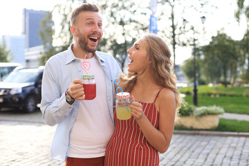 Beautiful young couple walking through the city street, smiling and drinking fresh cocktails