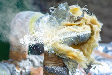 Damaged careless and unprofessionally insulated pipe with hot steam and water splashing out of the...