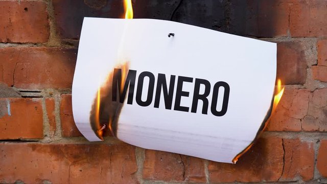 The inscription on a white A4 size sheet against the background of an orange brick wall. The paper with the black word Monero burns, smoke and turns into ashes. Business concept.