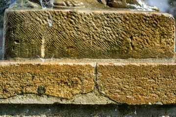 Stone, heavily textured pedestal about which drops of water are broken