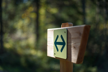 Hiking sign with two opposite arrows, mounted on a wooden signpost in the forest, with blurred...