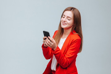 Naklejka premium girl in a red jacket is typing a message on the phone on a gray light background