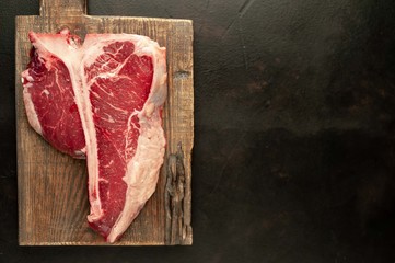 Raw t-bone steak with fresh herbs on a concrete or slate background, top view, place for text,