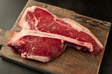 Raw t-bone steak with fresh herbs on a concrete or slate background, top view