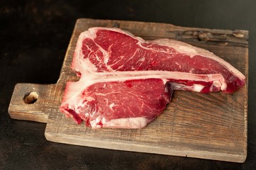 Raw t-bone steak with fresh herbs on a concrete or slate background, top view
