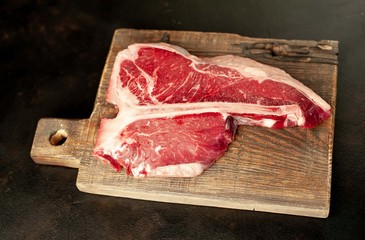 Raw t-bone steak with fresh herbs on a concrete or slate background, top view