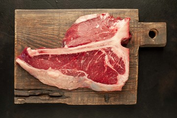 Raw t-bone steak with fresh herbs on a concrete or slate background, top view