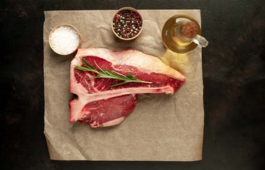 Raw t-bone steak with fresh herbs on a concrete or slate background, top view