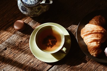 cup of  tea and croissant on wooden table