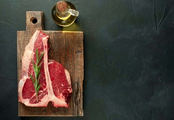 Raw t-bone steak with fresh herbs on a concrete or slate background, top view, place for text,