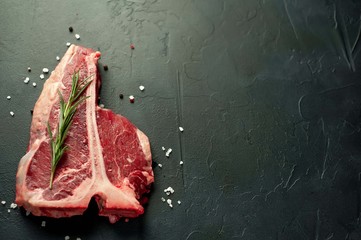 Raw t-bone steak with fresh herbs on a concrete or slate background, top view, place for text,