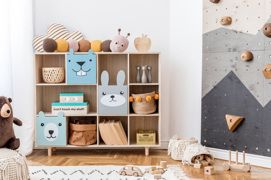 Stylish scandinavian child room with wooden cabinet, toys, boxes and plush teddy. White walls, Minimalistic home decor of playroom. Template. Modern home decor. Interior design. Kid room.