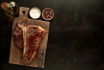 Grilled T-bone steak on a stone table. With rosemary and spices. Top view with copy space.