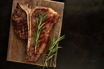 Grilled T-bone steak on a stone table. With rosemary and spices. Top view with copy space.