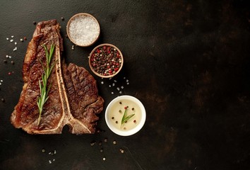 Grilled T-bone steak on a stone table. With rosemary and spices. Top view with copy space.