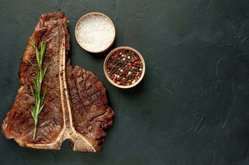 Grilled T-bone steak on a stone table. With rosemary and spices. Top view with copy space.