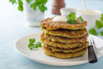 Zucchini fritters with fresh parsley and sour cream in plate on blue concrete background. Selective focus.