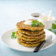 Zucchini fritters with fresh parsley and sour cream in plate on blue concrete background. Selective focus.