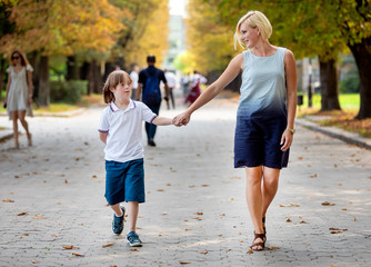 Happy special kid and his loving mom walk along an early autumn park path