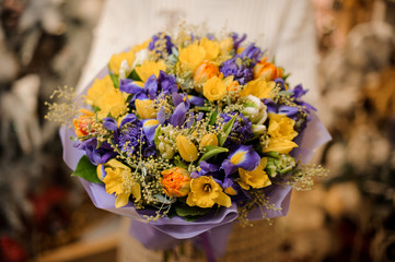 Girl holding a bouquet with purple and yellow flowers wrapped in violet paper