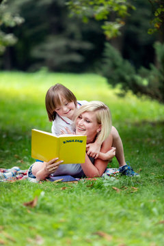 Mother and her special kid reading on a rug amidst a summer park lawn