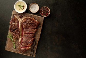 Grilled T-bone steak on a stone table. With rosemary and spices. Top view with copy space.