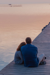 Fototapeta premium Woman lying on her boyfriend's shoulder while watching sunset. Loving couple at the lake.