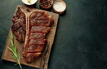Grilled T-bone steak on a stone table. With rosemary and spices. Top view with copy space.