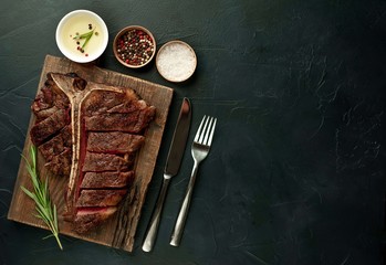Grilled T-bone steak on a stone table. With rosemary and spices. Top view with copy space.