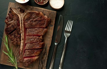 Grilled T-bone steak on a stone table. With rosemary and spices. Top view with copy space.
