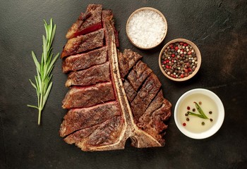 Grilled T-bone steak on a stone table. With rosemary and spices. Top view with copy space.