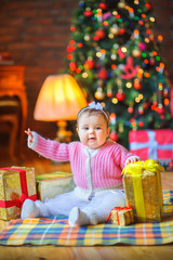 Fototapeta na wymiar A cute little girl is sitting on the floor next to presents and smiling. Holiday surprise. Christmas time