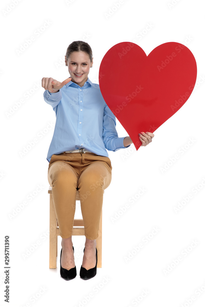 Wall mural young woman pointing finger and holding big red heart