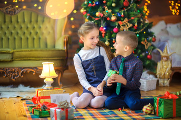 Fototapeta na wymiar Christmas time, cute children give presents while sitting on the floor near the festive Christmas tree