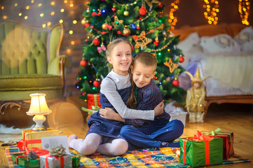 Fototapeta na wymiar Christmas time, cute children play cuddling and having fun sitting on the floor near the festive Christmas tree