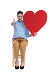 Fototapeta na wymiar happy young woman holding heart and making thumbs up sign